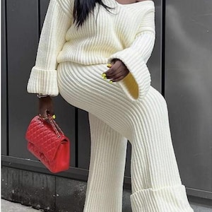 May include: A white knitted sweater and pants set with a wide leg silhouette and cuffed sleeves and pant legs.