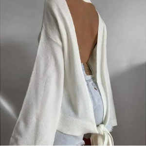 Könnte beinhalten: Weißer Strickpullover mit tiefem Rücken und einer Schleife im Rücken.