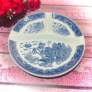 May include: A white divided serving plate with a blue and white Willow pattern design. The plate has three sections and a detailed landscape scene with buildings, bridges, and boats. The rim features a decorative border.