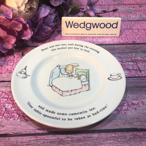 Puede incluir: Un plato de cerámica blanco con una ilustración de Peter Rabbit. El plato presenta una cita del libro: "Peter was not very well during the evening. His mother put him to bed. and made some camomile tea: 'One table-spoonful to be taken at bed-time."