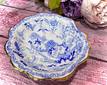 May include: A white and blue ceramic dish with a scalloped edge and gold trim. The dish features a blue and white landscape design. The dish is likely used for serving or display.