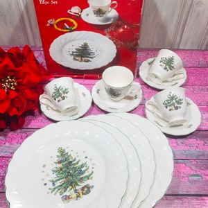 May include: A 12-piece Christmas dinnerware set by Nikko featuring a green Christmas tree design on white plates and cups. The set includes four dinner plates, four salad plates, and four teacups and saucers.