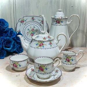 May include: A white tea set with a floral pattern. The set includes a teapot, creamer, sugar bowl, cup and saucer, and a square plate.