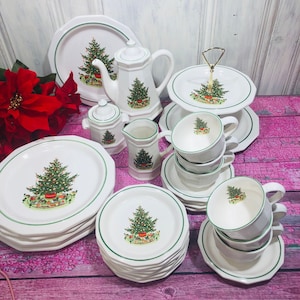 May include: A white Christmas-themed dinnerware set with a green trim. The set includes plates, cups, saucers, a teapot, a creamer, a sugar bowl, and a two-tiered serving tray. Each piece features a decorated Christmas tree design.