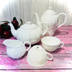 Könnte beinhalten: Ein weißes Teeservice mit Blattdesign. Das Set beinhaltet eine Teekanne, eine Milchkännchen, eine Zuckerdose und zwei Teetassen.