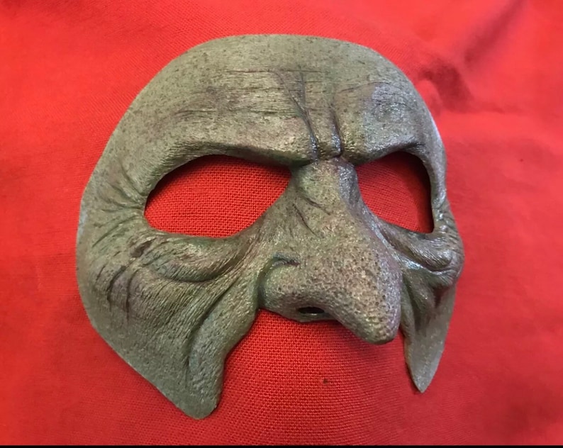 May include: A green, textured, molded plastic mask with a large, bulbous nose and eye holes. The mask is designed to resemble a grotesque, aged face.
