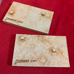 May include: Two beige display stands with the words "Indiana Jones" printed on them. Each stand has two small round holes.