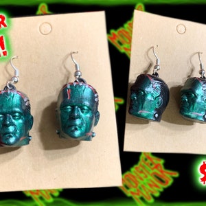 May include: A pair of green and black Frankenstein head dangle earrings. The earrings are on a brown card with the text "NEW FOR 2024!" and "$15.00".