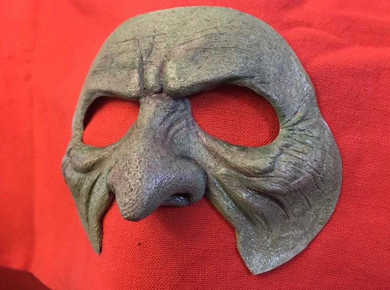 May include: A green, textured, and detailed mask with a large, prominent nose and eye holes. The mask is made of a material that resembles leather or rubber.