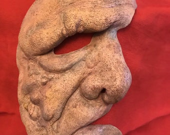 May include: A detailed, textured, beige-colored mask with a large nose and a wide mouth. The mask is made of a soft, pliable material and has a realistic appearance.
