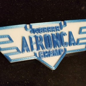 May include: A white and blue plastic keychain with an airplane wing design and the text "AERONCA CHAMP" in blue letters.