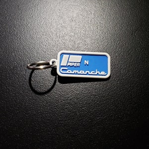 May include: Blue and white plastic keychain with the text "Piper N Comanche" on it.