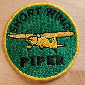 May include: A green and yellow embroidered patch with the text "SHORT WING PIPER" and a yellow airplane illustration.