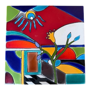 May include: A square ceramic tile featuring a vibrant, abstract landscape design with bold blocks of red, blue, green, yellow, and black. The scene includes a stylized yellow flower, a sun-like motif, and geometric shapes forming a house-like structure.