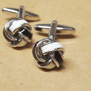 May include: Two silver cufflinks with a knot design. The knots are black and white with a white enamel stripe.