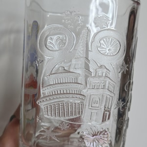 May include: Clear glass tumbler with embossed architectural designs, including a pagoda, tower, and other structures. The glass features star and swirl accents, creating a decorative and detailed design. A unique addition to any glassware collection.
