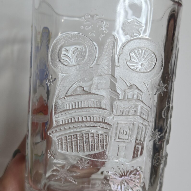 May include: Clear glass tumbler with embossed architectural designs, including a pagoda, tower, and other structures. The glass features star and swirl accents, creating a decorative and detailed design. A unique addition to any glassware collection.