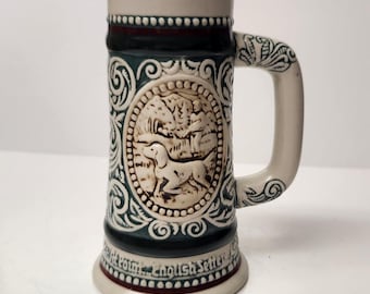 Puede incluir: Una jarra de cerveza de cerámica con un diseño verde y blanco. La jarra presenta una imagen en relieve de un perro corriendo por el bosque. El texto "At Point... English Setter" es visible en la parte inferior de la jarra.