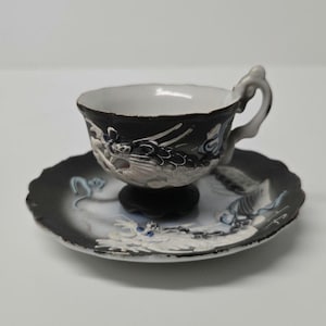 Peut inclure: Une tasse à thé et une soucoupe en noir et blanc avec un motif de dragon. La tasse et la soucoupe sont décorées d'un dragon blanc sur fond noir.