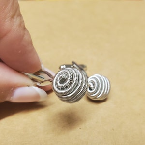 May include: A pair of silver cufflinks with a unique, coiled design. Each cufflink is a sphere made of tightly wound wire.