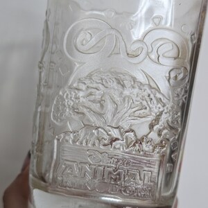 May include: Clear glass tumbler with embossed design featuring a tree, animals, and the text "Disney's Animal Kingdom". The glass has a slightly flared shape and is partially filled.