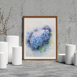 May include: A watercolor painting of a blue hydrangea flower in a wooden frame. The painting is displayed on a wall with white vases and a feather.