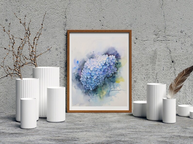 May include: A watercolor painting of a blue hydrangea flower in a wooden frame. The painting is displayed on a wall with white vases and a feather.
