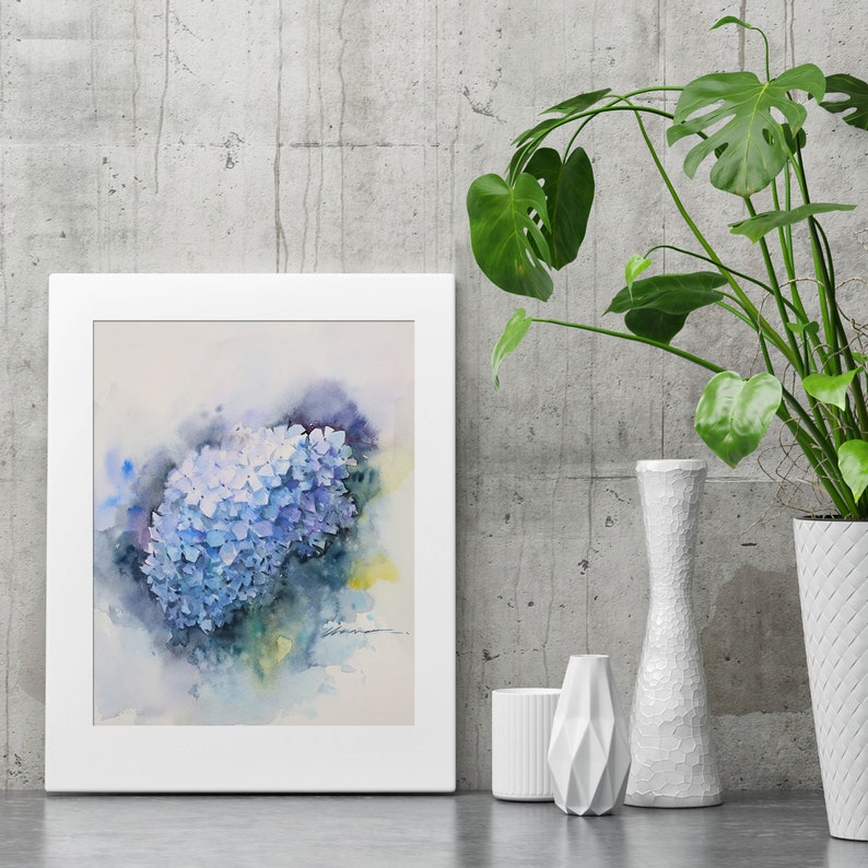 May include: A watercolor painting of a blue hydrangea flower in a white frame. The painting is set against a gray concrete wall with a green plant in a white vase.