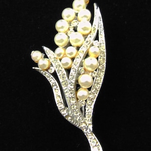 May include: A silver brooch featuring a stylised flower design with pearl-like beads and rhinestones.