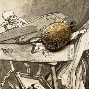 May include: An antique gold locket with an engraved floral design. The locket is resting on a vintage illustration of a skeleton in a coffin. The illustration includes the text "Come to Life Again."