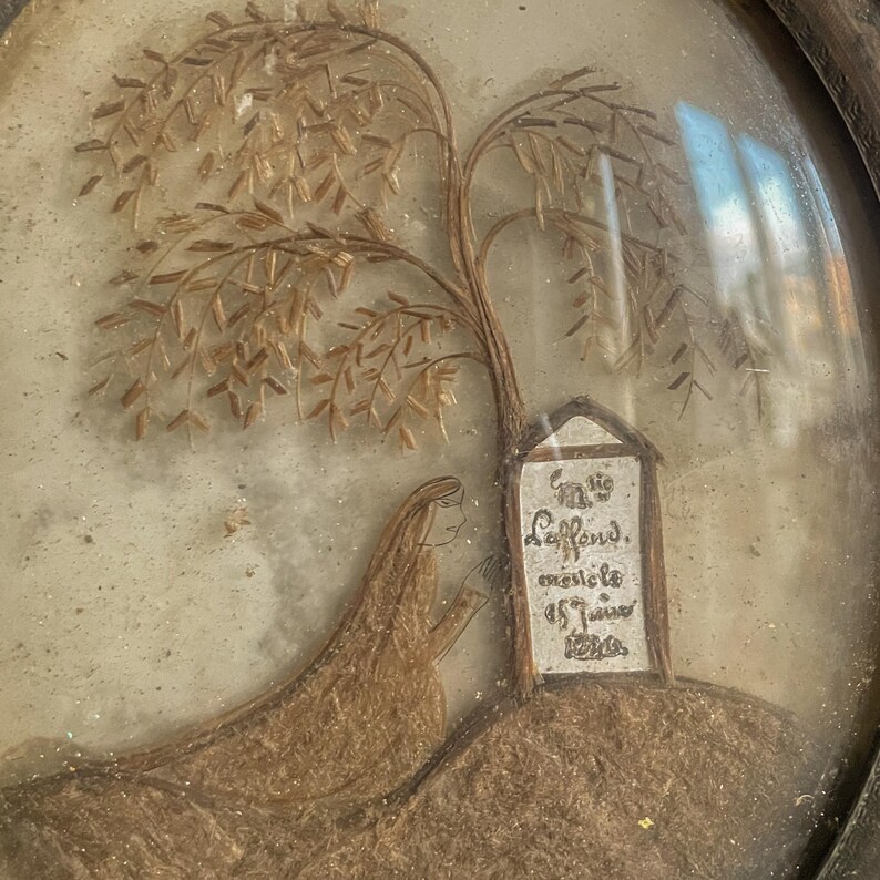 Puede incluir: Una obra de arte enmarcada hecha de cabello humano que representa a una mujer de pie bajo un &aacute;rbol con una l&aacute;pida que dice "In lie Lafond, meilete as 17ans 1820."