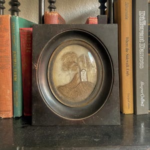 Puede incluir: Una silueta en blanco y negro enmarcada de un &aacute;rbol y una peque&ntilde;a casa en una colina. El marco es de madera oscura y tiene una cubierta de vidrio. La imagen es de estilo vintage.