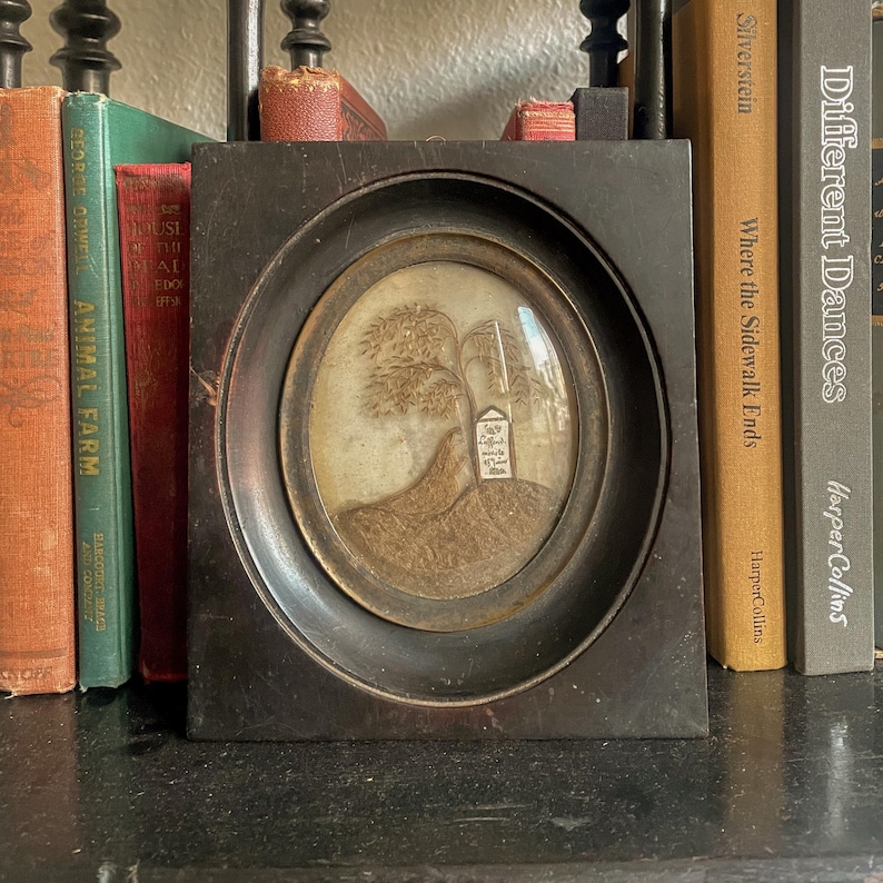 Puede incluir: Una silueta en blanco y negro enmarcada de un &aacute;rbol y una peque&ntilde;a casa en una colina. El marco es de madera oscura y tiene una cubierta de vidrio. La imagen es de estilo vintage.