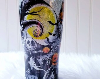 May include: A black and white tumbler with a glitter finish features a Nightmare Before Christmas design. The design includes Jack Skellington, Sally, and other characters from the movie. The tumbler has a silver lid and a clear straw.