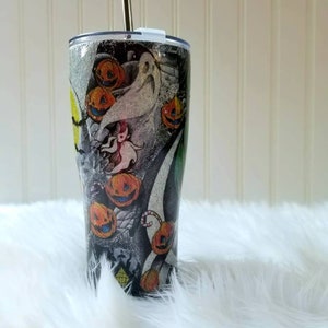 Op de afbeelding: Een zwarte en zilveren roestvrijstalen beker met een Halloween-thema met Jack Skellington en pompoenen. De beker heeft een rietje en een deksel.