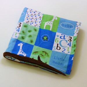 May include: A blue and green baby blanket with a brown border. The blanket features a giraffe, a frog, a tree, and the words "baby", "Little Buddy", and "a3c6b2145".