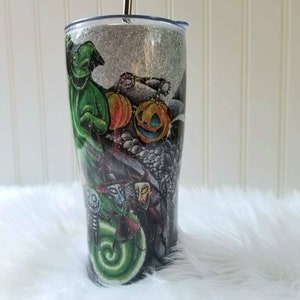 Op de afbeelding: Een zwarte en groene glitterbeker met een Nightmare Before Christmas-ontwerp. Het ontwerp toont Jack Skellington, Sally, Oogie Boogie en de burgemeester.
