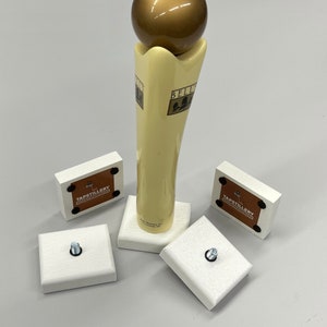 May include: A set of four white wooden bases with a gold-colored beer tap handle. The bases have a brown label with the text "Tapstillery" on them. The tap handle has a gold-colored ball on top and the text "Bell's" on the side.