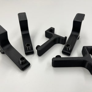 May include: A collection of six black, 3D-printed brackets. Each bracket has a curved arm with a flat top and a threaded hole for a screw. The brackets are arranged on a white surface.