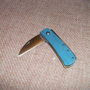 May include: A blue pocket knife with a silver blade and a textured blue handle. The knife is open and the blade is partially extended.