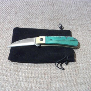 May include: A green and silver pocket knife with a wooden handle, in a black velvet pouch.