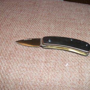 May include: A black folding pocket knife with a gold accent on the handle. The blade is partially open.