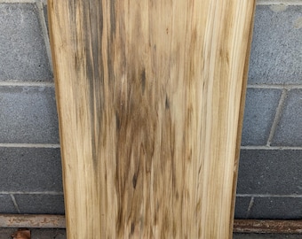 May include: A large piece of wood with a natural live edge. The wood has a light brown color with dark brown streaks throughout.