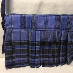 May include: A blue and black plaid crossbody bag with a pleated bottom. The bag has a zipper closure and a strap.