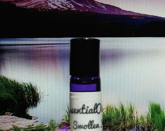 Peut inclure: Petite bouteille de roll-on d'huile essentielle bleu foncé avec un bouchon noir. L'étiquette indique "Essential Oils, Swollen Feet, Ankles Relief". En arrière-plan, une chaîne de montagnes et un lac.