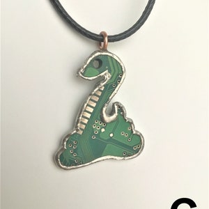 May include: A green circuit board snake pendant necklace with a black cord. The pendant is made from a recycled circuit board and has a silver finish.