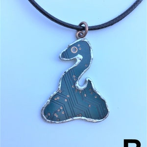 May include: A necklace with a black cord and a pendant shaped like a snake made from a circuit board. The pendant is silver with copper accents and has a green circuit board design.