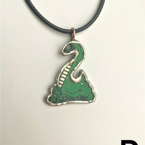 May include: A green circuit board pendant necklace with a snake design. The pendant is attached to a black cord.