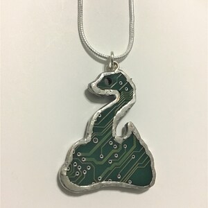 May include: A silver chain necklace with a pendant shaped like a coiled snake. The snake is made of a green circuit board.