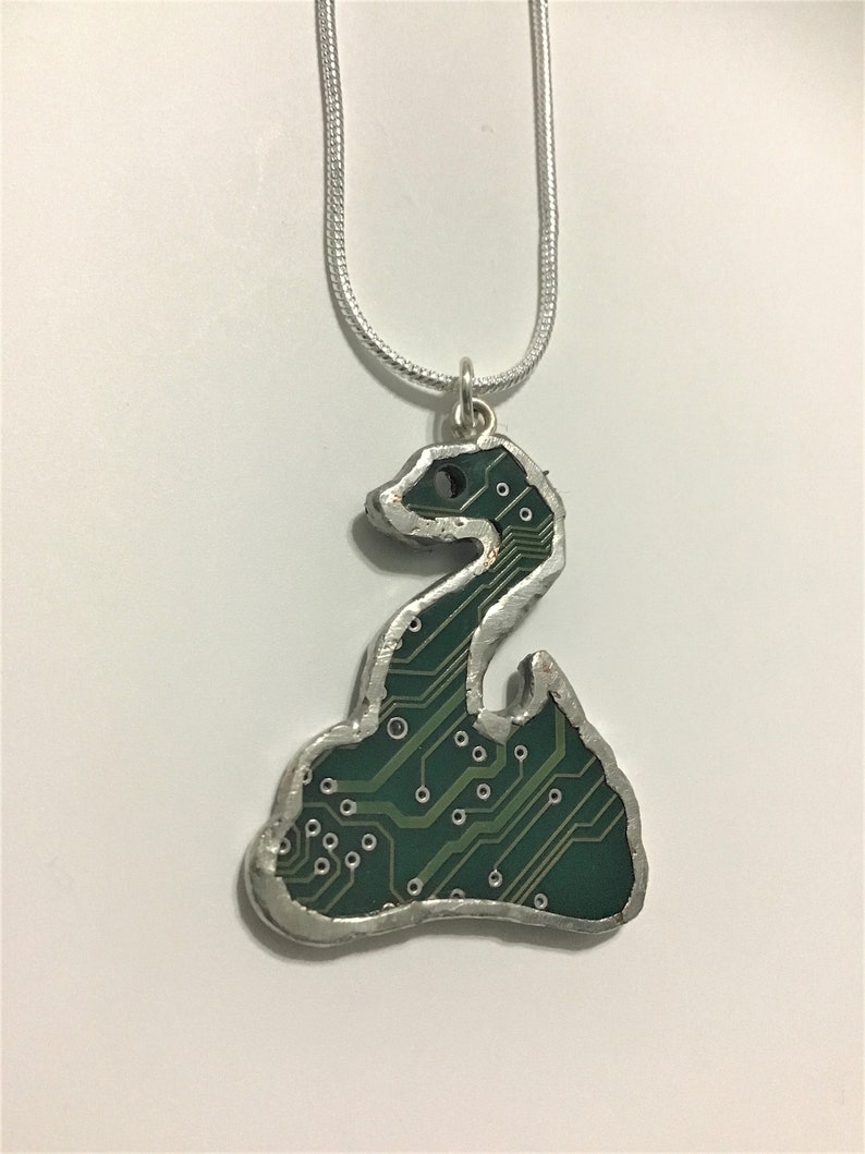 May include: A silver chain necklace with a pendant shaped like a coiled snake. The snake is made of a green circuit board.